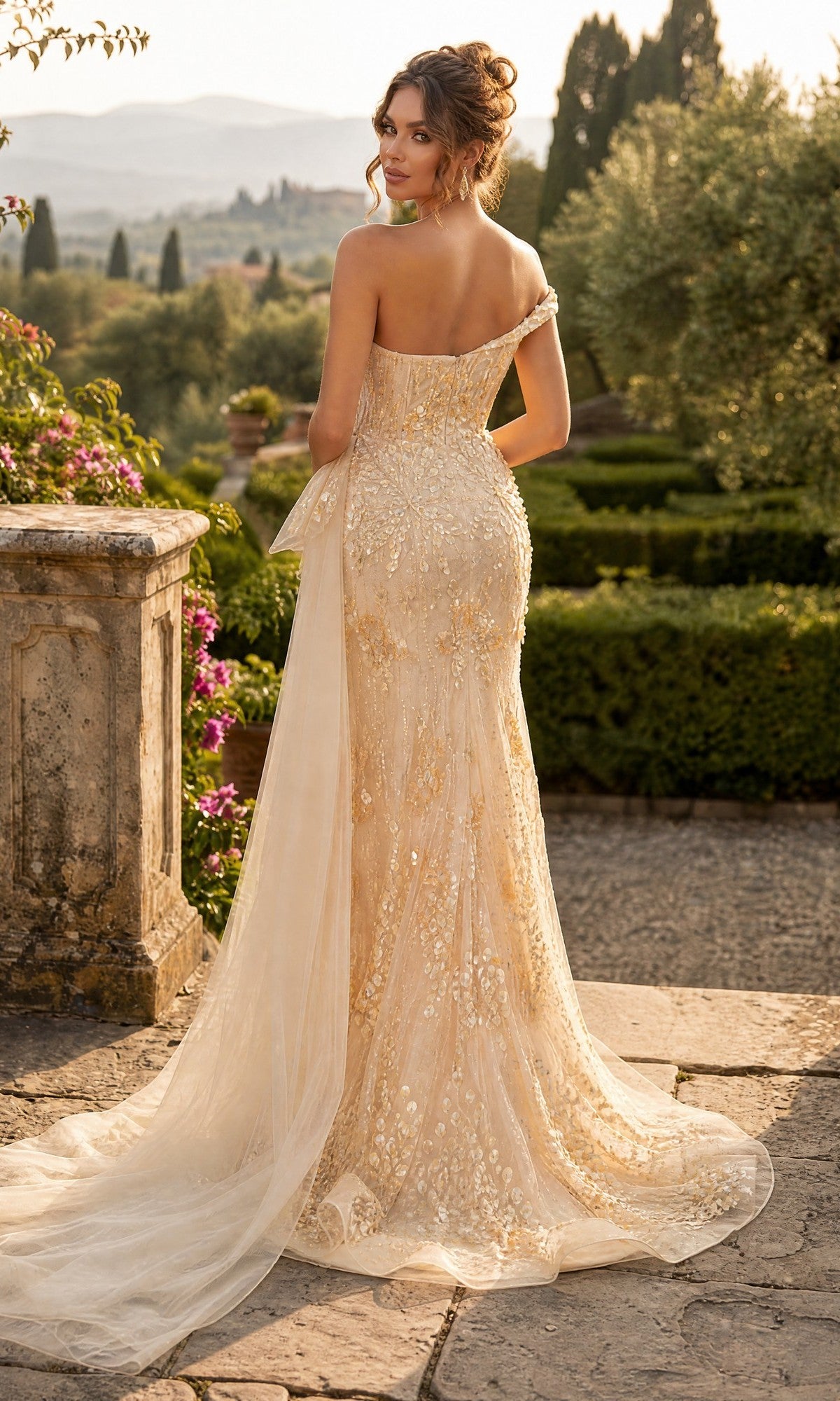 Wearing the Long Formal Dress: Chicas YG5035—an off-shoulder, fitted cream-colored gown with floral details—a woman stands outdoors on a stone terrace, facing away, surrounded by greenery and distant hills in the background.